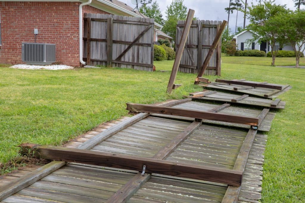 Damaged wooden fence collapsed across a grassy yard, with broken and leaning fence panels.